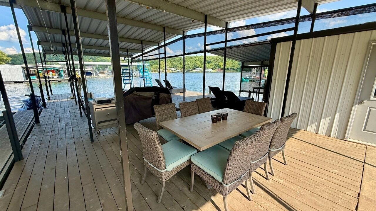 A covered outdoor dining area with a table and chairs, overlooking a body of water.