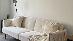 A beige sofa with a textured throw blanket and two pillows, positioned against a plain wall with a floor lamp to the left. - Nottingham 2-bed House, Sleeps 4, Pet Friendly (Nottingham)