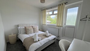 A neatly arranged bedroom with a bed, bedside tables, a chair, and a window with curtains. - Nottingham 2-bed House, Sleeps 4, Pet Friendly (Nottingham)