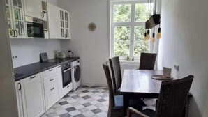 A compact kitchen with white cabinets, a black countertop, a washing machine, and a dining area with a table and chairs. - Golden apartment on the estate (Nordstemmen)