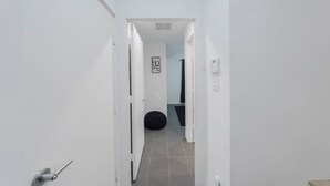 Een smalle gang met witte wanden en grijs betegelde vloer, die leidt naar een kamer met een zwarte kruikzitzak en een bordje 'HOME' in een lijst aan de muur.