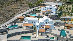 A modern resort with multiple swimming pools, outdoor seating areas, and a stone facade. - 180 SUITES (Santorini)