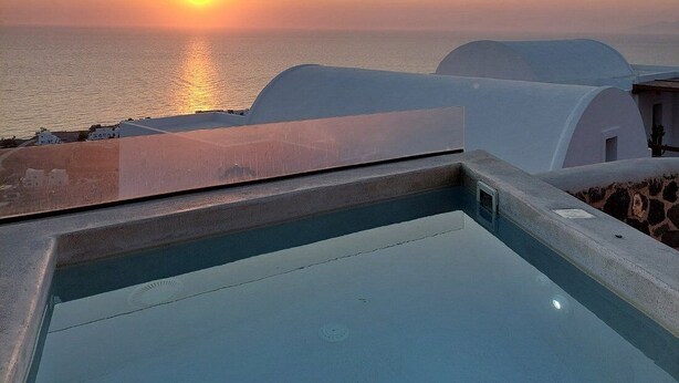 A pool with a view of the sunset over the sea, white buildings, and a clear sky. - 180 SUITES (Santorini)