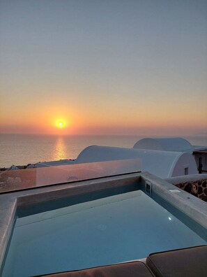 A pool with a view of the sunset over the sea, white buildings, and a clear sky. - 180 SUITES (Santorini)