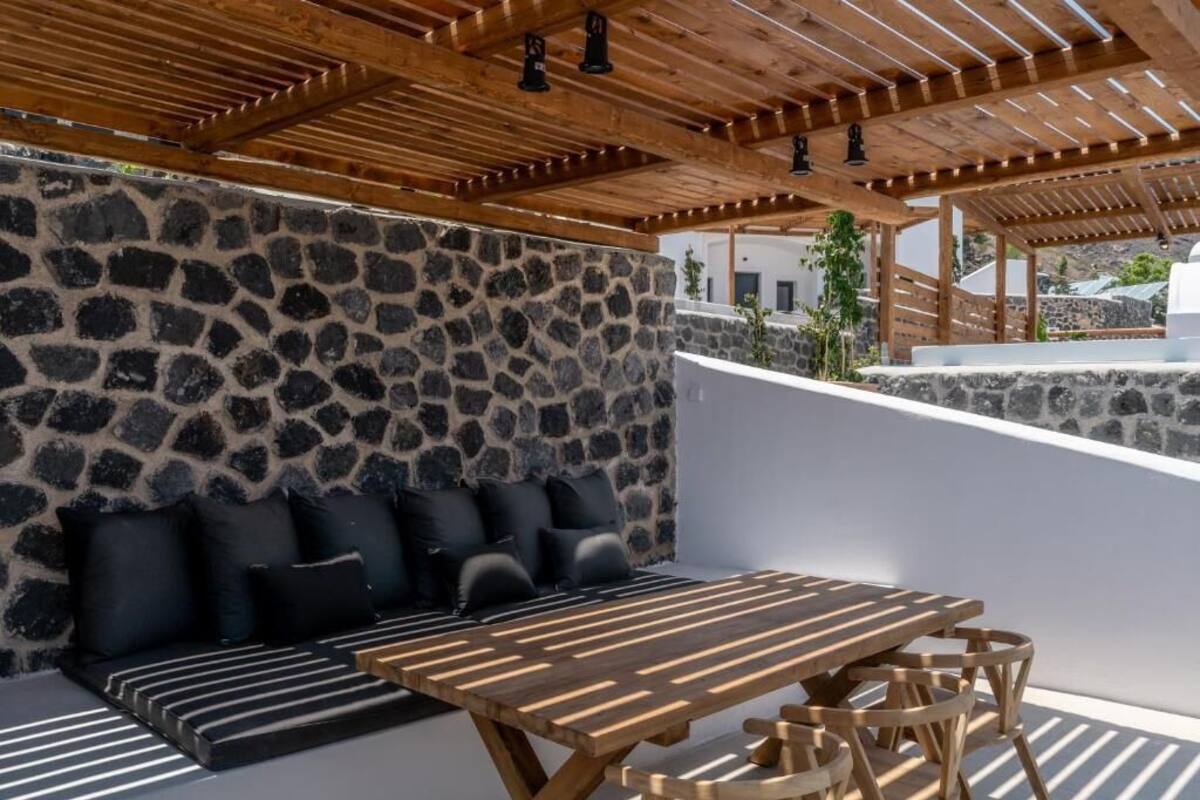 A stone wall with a wooden ceiling, a sofa with black cushions, and a wooden table with chairs.