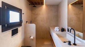 A modern bathroom with a large mirror, a built-in sink, and a shower area. - 180 SUITES (Santorini)