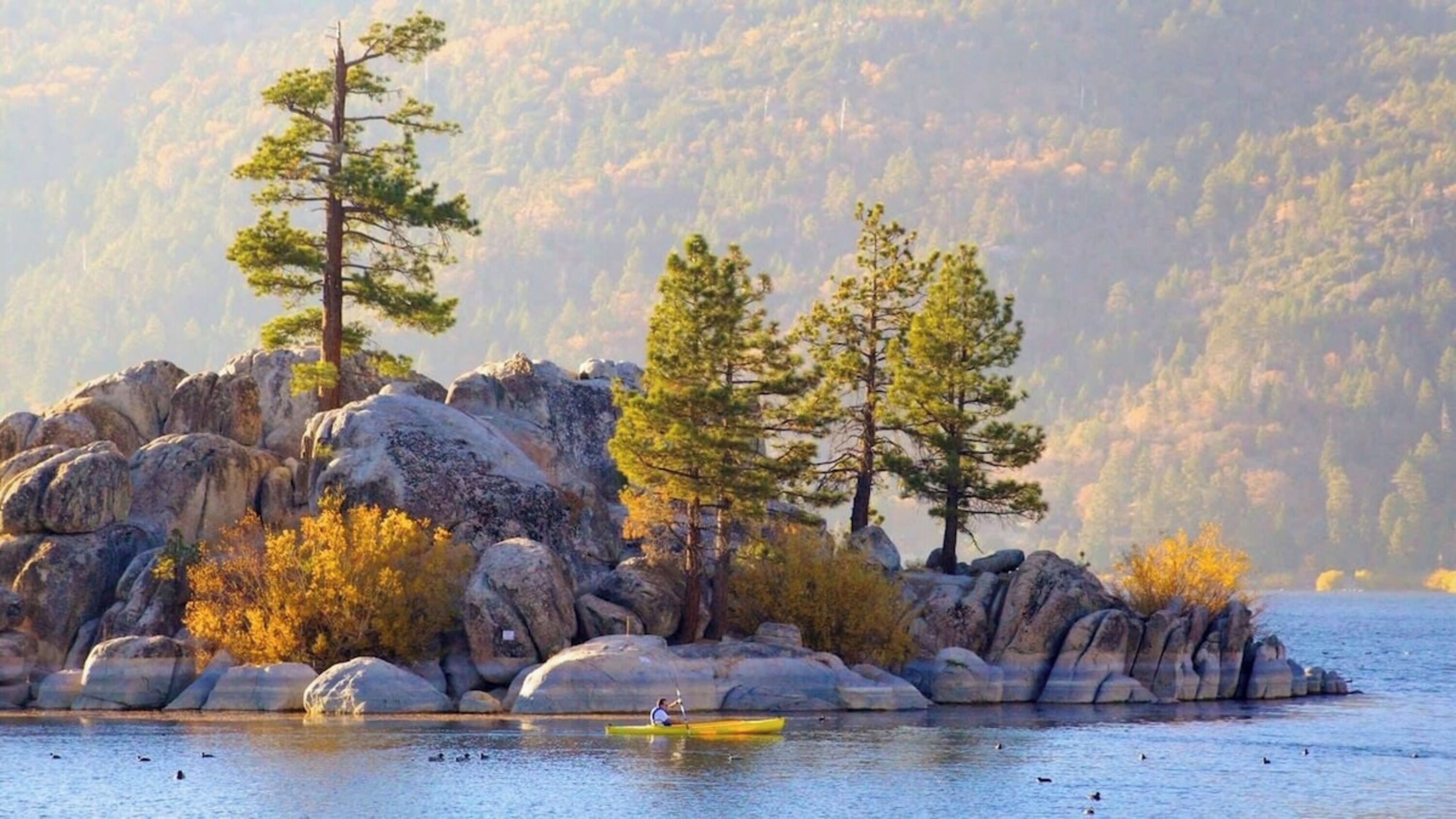 A calm lake with a rocky island featuring large boulders and several trees.