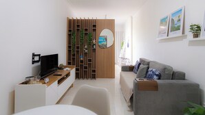 A modern living room with a grey sofa, a wooden entertainment unit, a TV, and a decorative mirror. - SUH Botafogo 04 Pão de Açúcar View (Rio de Janeiro)