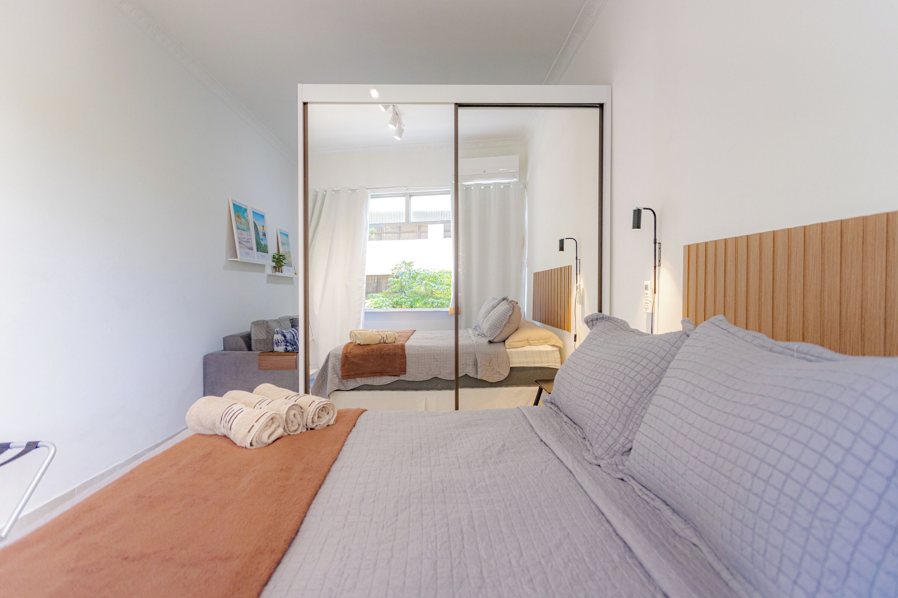 A modern bedroom with a large bed, a wooden headboard, a bedside table, and a view of a balcony.