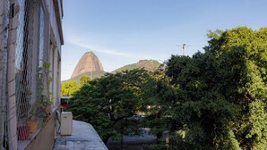 A building with a chain-link fence, a concrete structure, and a view of a mountain. - SUH Botafogo 04 Pão de Açúcar View (Rio de Janeiro)