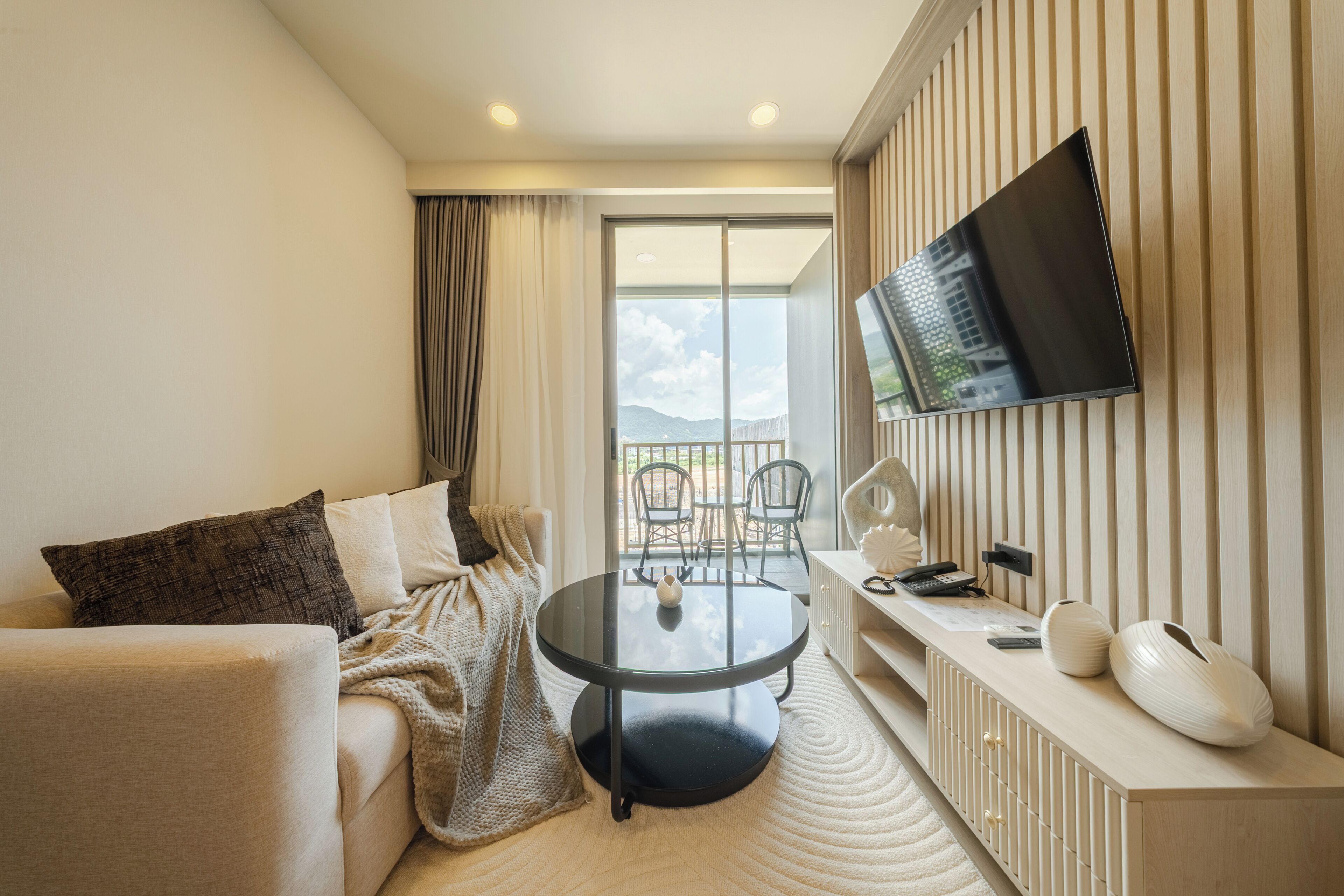Een hotelkamer met een bank, een ronde tafel, een aan de muur bevestigde televisie en uitzicht op de omgeving.