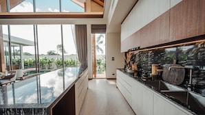 A modern kitchen with a large island, a built-in stove, and a view of a pool and greenery. - The Ozone Residences Bangtao (Choeng Thale)