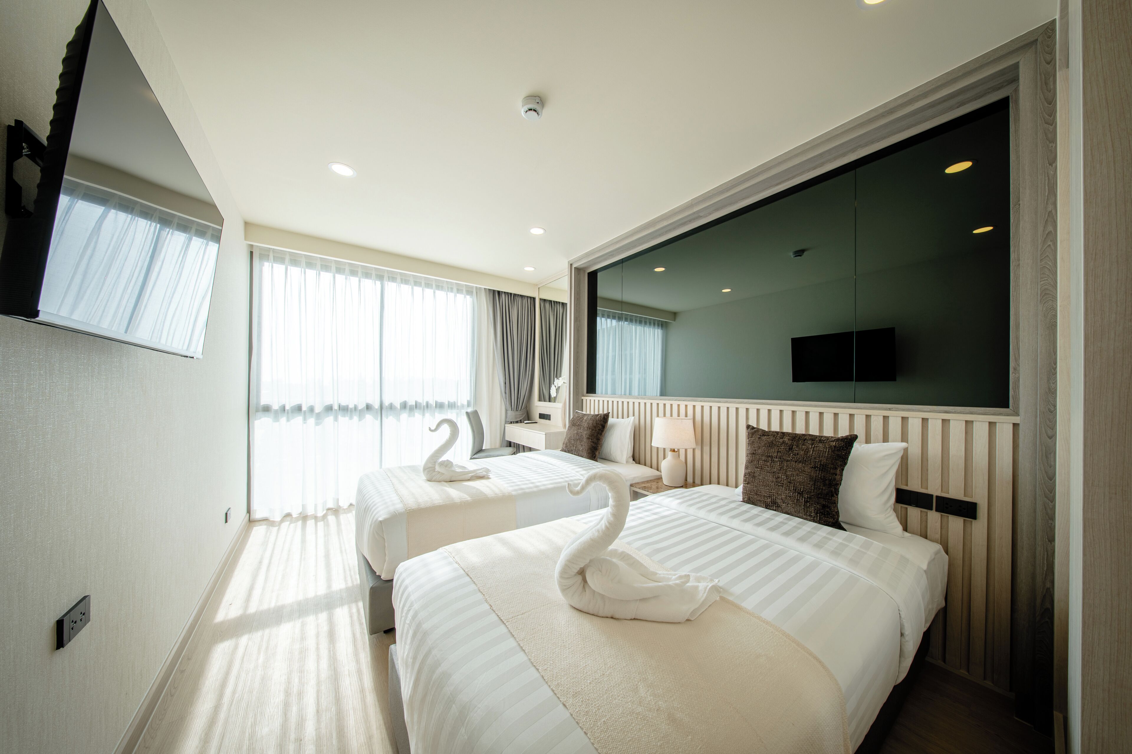 A hotel room with two beds, a TV, a large window with curtains, and a mirror.