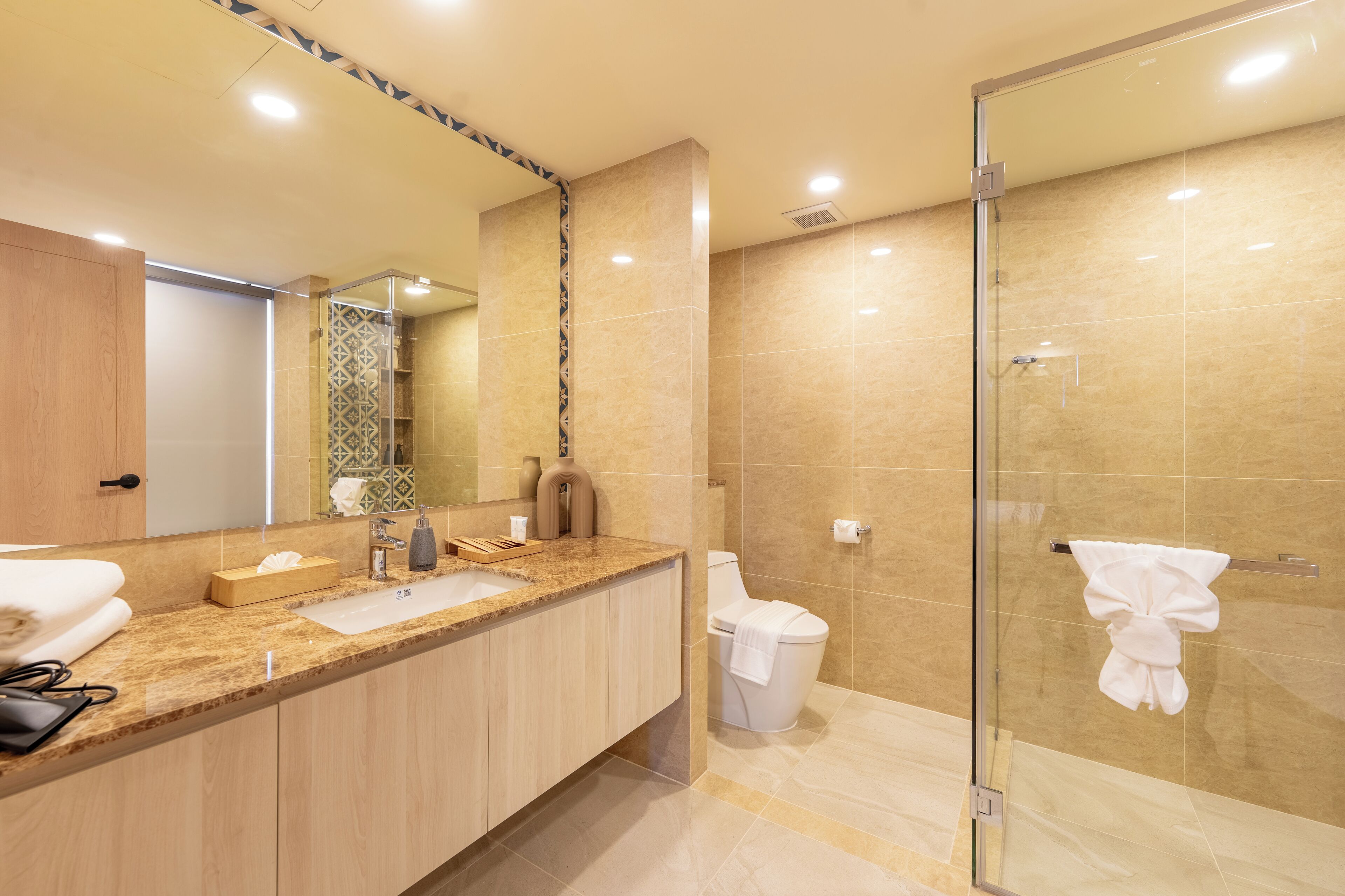 A modern bathroom with a large mirror, a sink, a toilet, and a glass-enclosed shower area.