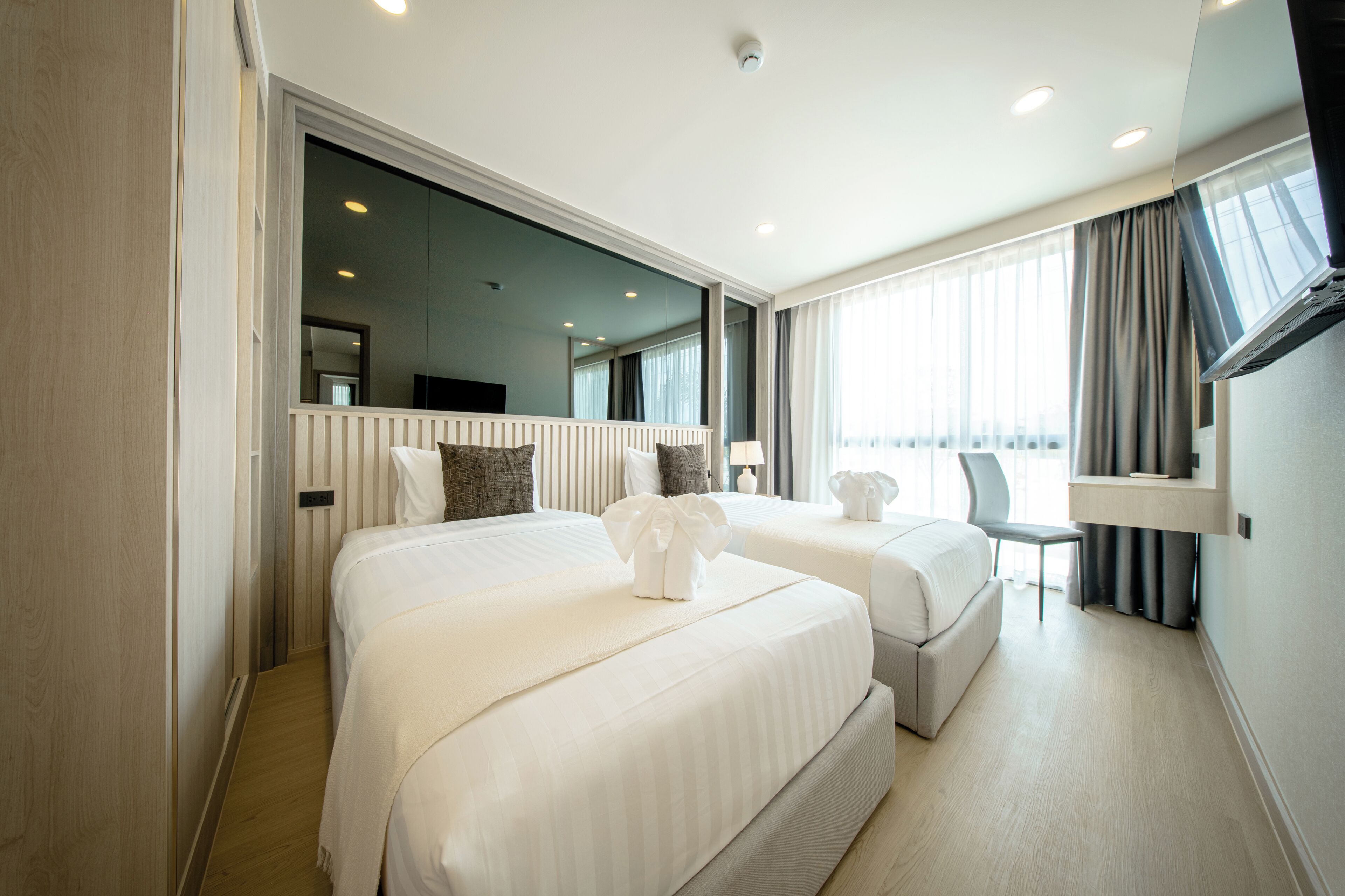 Une chambre d’hôtel avec deux lits, un bureau, une chaise, une grande fenêtre et un miroir.