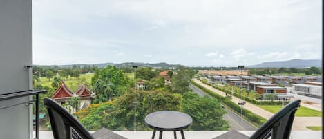 A balcony with two chairs and a small table, offering a view of a residential area with houses and greenery.