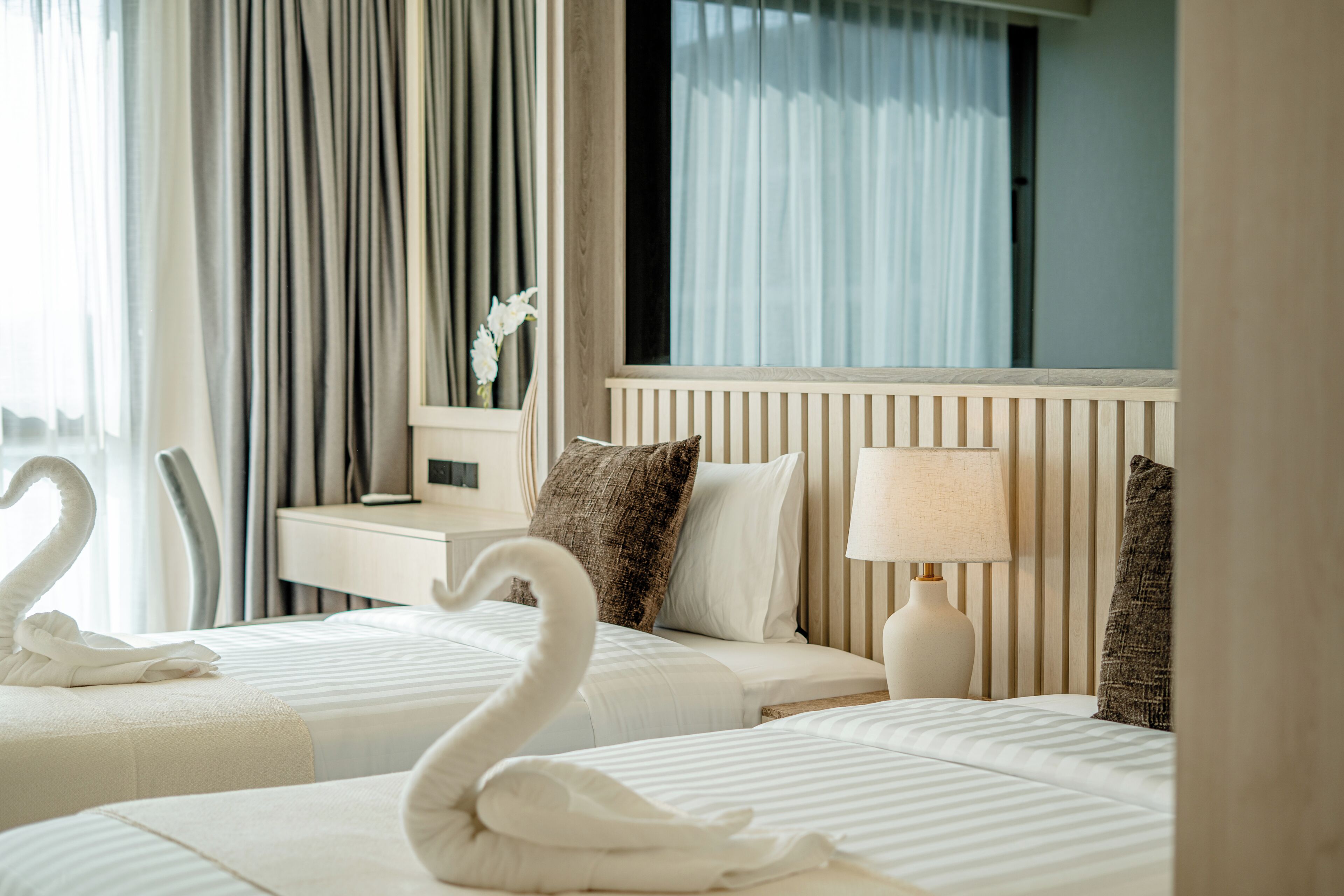 A hotel room with two beds, a nightstand, a lamp, and a mirror.