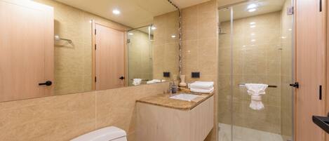 Un baño moderno con inodoro, lavamanos y cabina de ducha con mampara de vidrio.