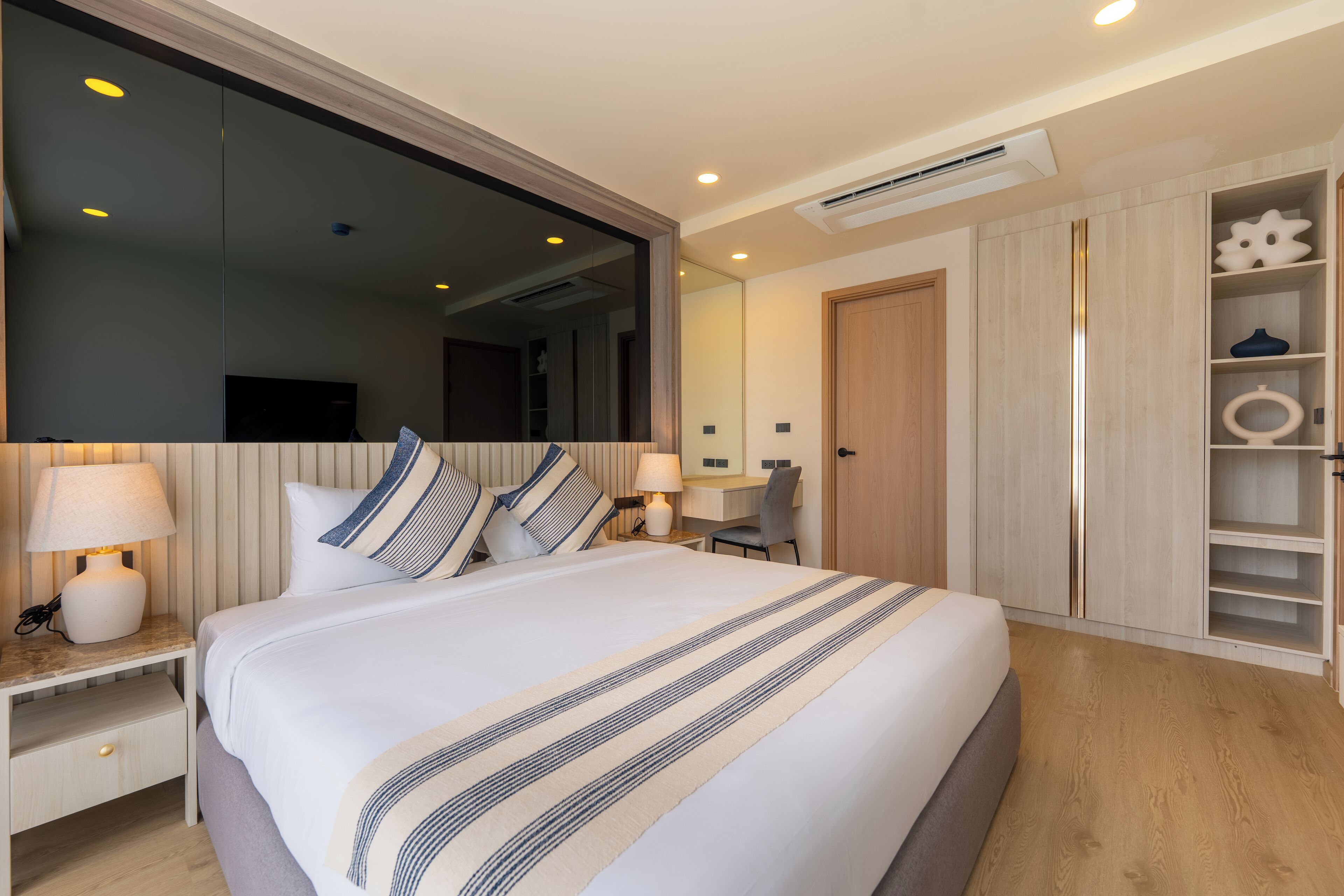 Une chambre d’hôtel moderne, dotée d’un grand lit, de tables de chevet avec des lampes, d’un miroir, d’un bureau et d’une armoire.