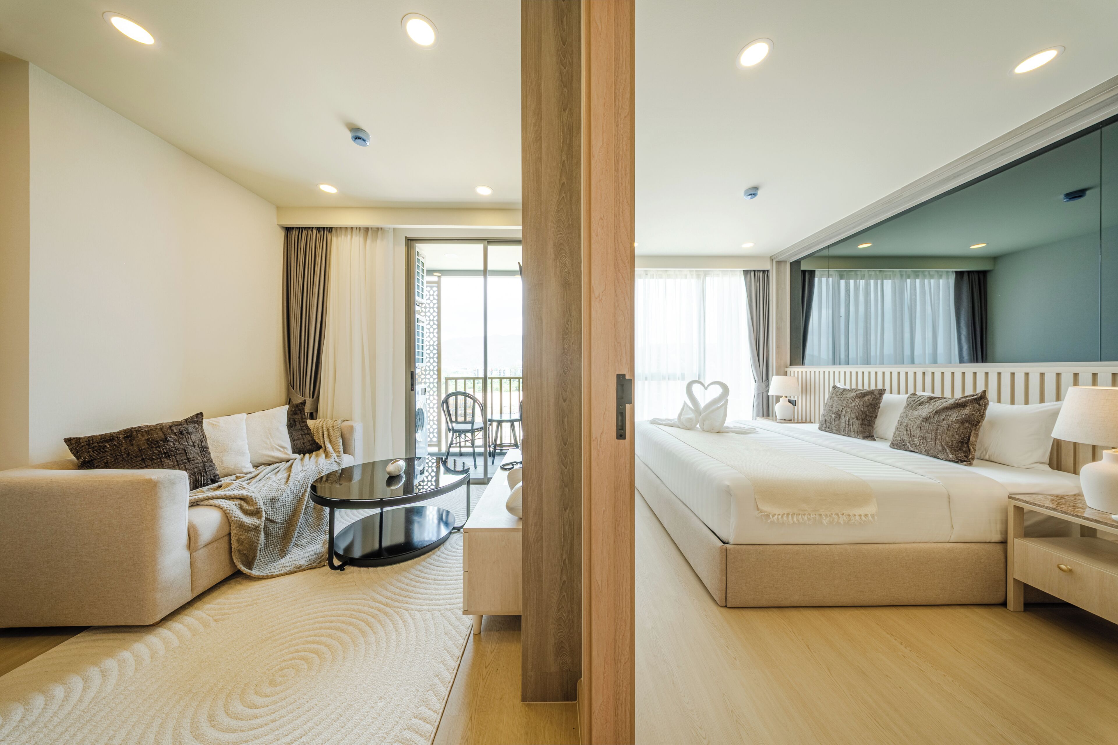 Une chambre d’hôtel moderne, dotée d’un canapé, d’une petite table ronde, d’un lit avec une tête de lit et d’une grande fenêtre avec des rideaux.