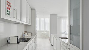 A modern kitchen with white cabinetry, a stainless steel sink, and a breakfast bar. There is a small dining area with a table and chairs in the background.