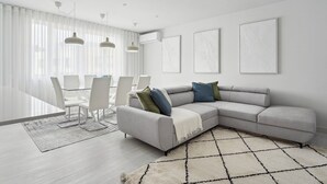A modern living room with a grey sectional sofa, white chairs, and a glass dining table.