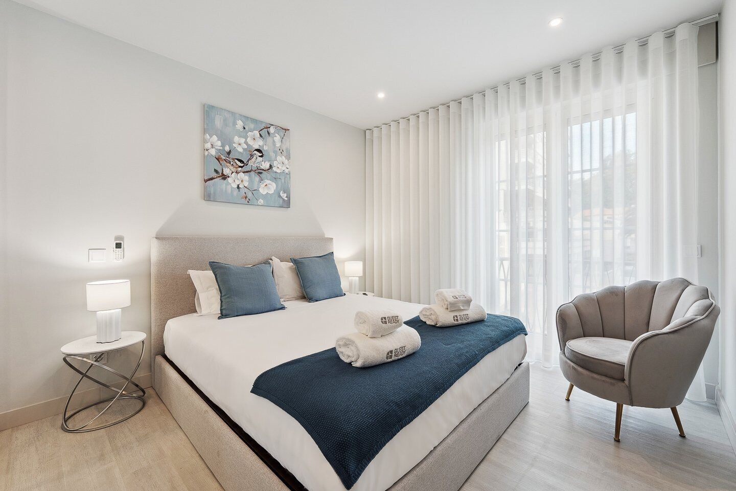 Una habitación de hotel moderna con una cama grande, una silla, un cuadro y vistas a la ciudad.