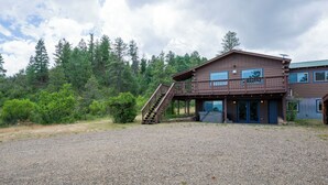 A two-story building with a staircase leading to the upper level, surrounded by a gravel driveway and dense forest.
