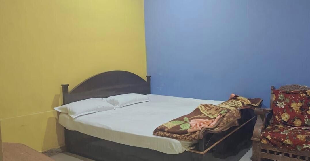 Een eenpersoonsbed met een wit laken en een bed met een patroon, een houten hoofdbord en een stoel met een bloemendesign.