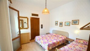 Ein Schlafzimmer mit zwei Betten, einem Holzschrank, einem Spiegel und einer Deckenleuchte.