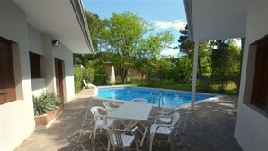 Eine überdachte Terrasse mit Pool, Gartenmöbeln und Steinboden.