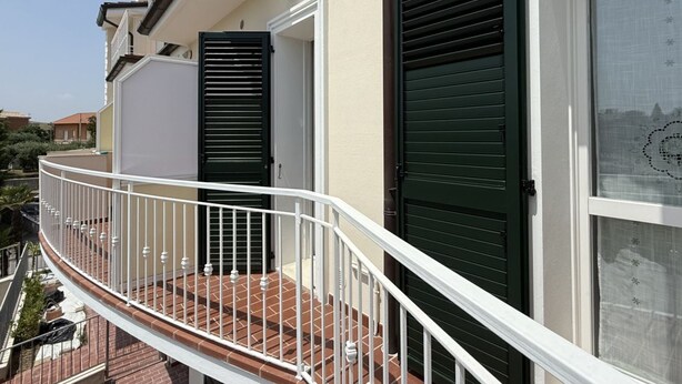 A balcony with a white railing, a door with a green shutter, and a window with a patterned curtain. - P068 - Porto Recanati, new two-room apartment with panoramic terrace (Porto Recanati)