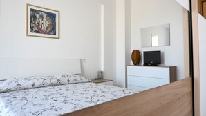 A bedroom with a bed, a nightstand, a dresser, a television, and a painting on the wall. - P068 - Porto Recanati, new two-room apartment with panoramic terrace (Porto Recanati)