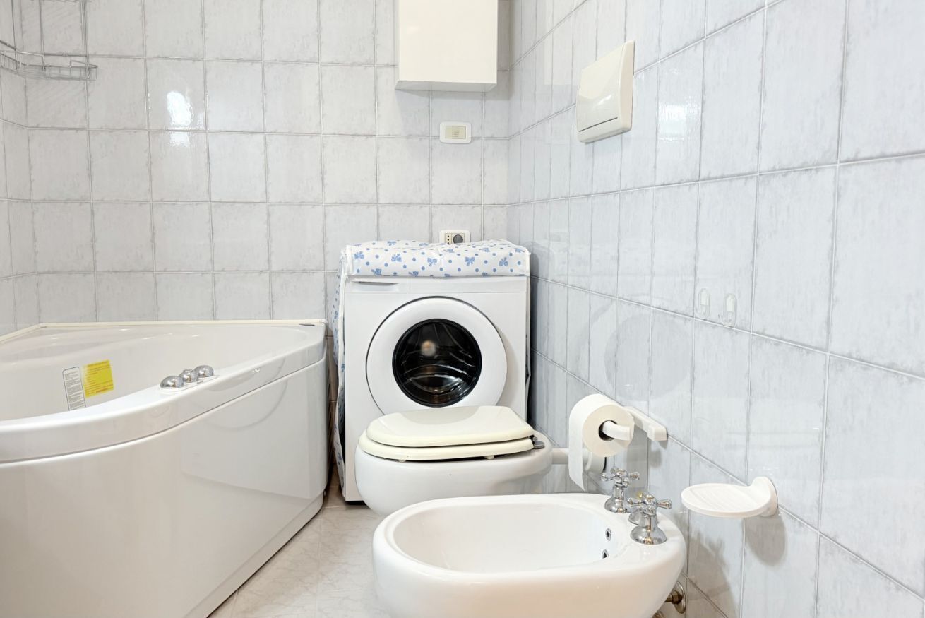 A bathroom with a bathtub, washing machine, toilet, and sink.