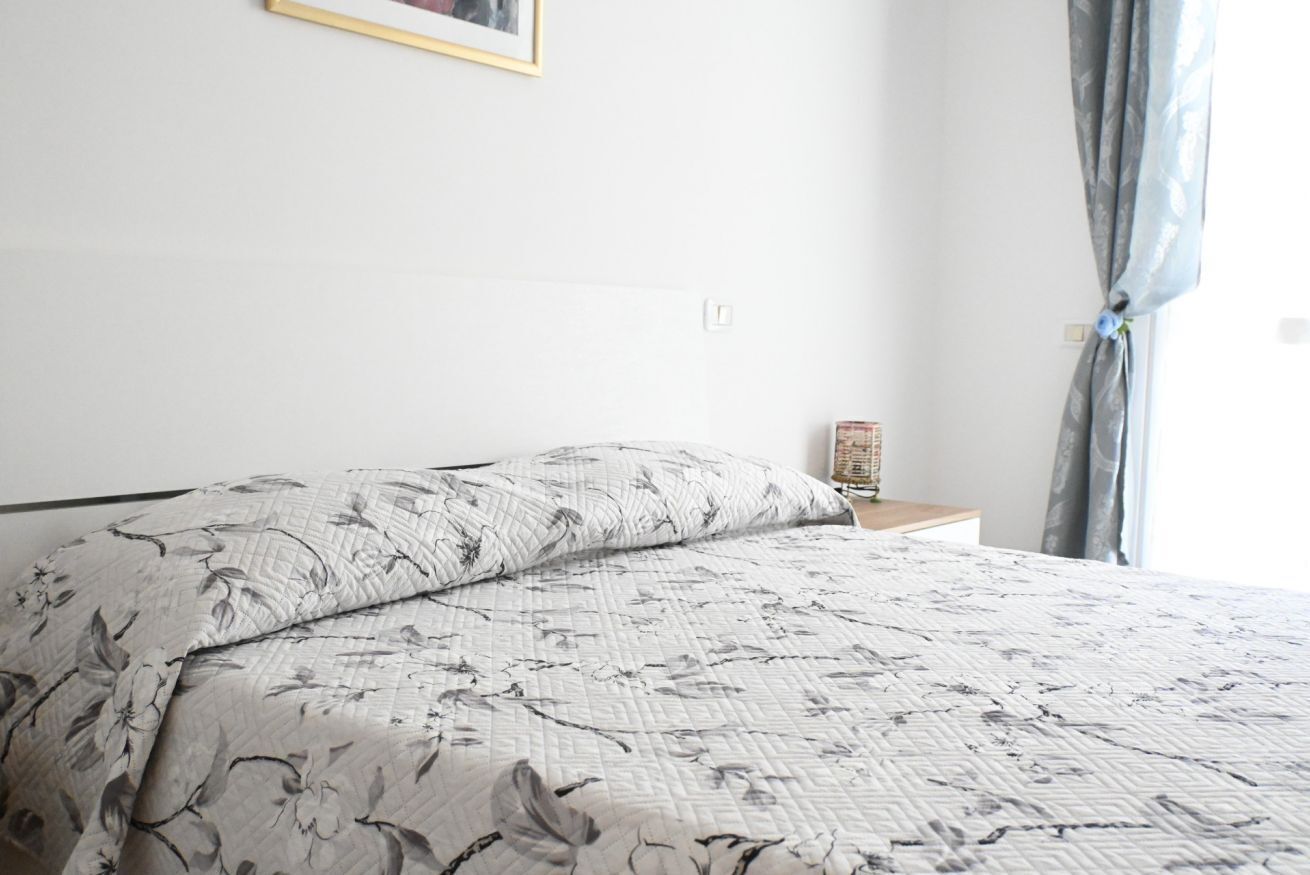 A bed with floral bedding, a bedside table with a lamp, and a window with curtains.