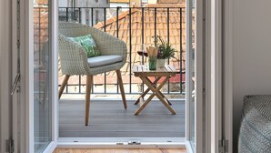 Un balcón con una silla de mimbre, una mesita con una planta y vistas a edificios.