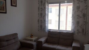 A living room with two sofas, a small table with a vase, and a window with floral curtains. - Large apartment, sea view with Wi-Fi (Guilhermina Praia Grande)