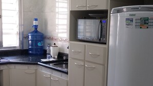 A kitchen with white cabinets, a white refrigerator, a microwave, a water dispenser, and a large water jug. - Large apartment, sea view with Wi-Fi (Guilhermina Praia Grande)