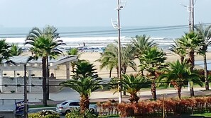 Une vue sur la plage, avec des palmiers, une voiture blanche et un bâtiment sur lequel on peut voir une enseigne.