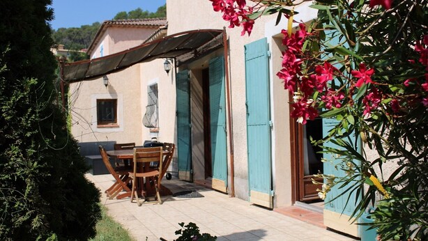 A patio with a wooden table and chairs, a covered area, and a building with blue shutters. - Villa la colle sur loup close to the sea, ideal family, near village (La Colle-sur-Loup)