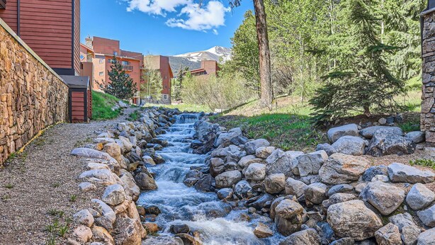 A stream flowing through a rocky bed, surrounded by a stone wall and a building with a red facade. - Spacious Ski-In Condo in the Heart of Breckenridge! (Breckenridge)
