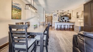 A spacious dining area with a long table and chairs, a kitchen in the background, and a living area with a leather couch. - Spacious Ski-In Condo in the Heart of Breckenridge! (Breckenridge)