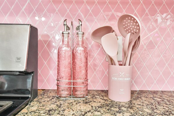 Una encimera de cocina con un electrodoméstico de acero inoxidable, dos botellas de vidrio con tapas metálicas y un recipiente rosa para utensilios con cucharas y espátulas de madera.