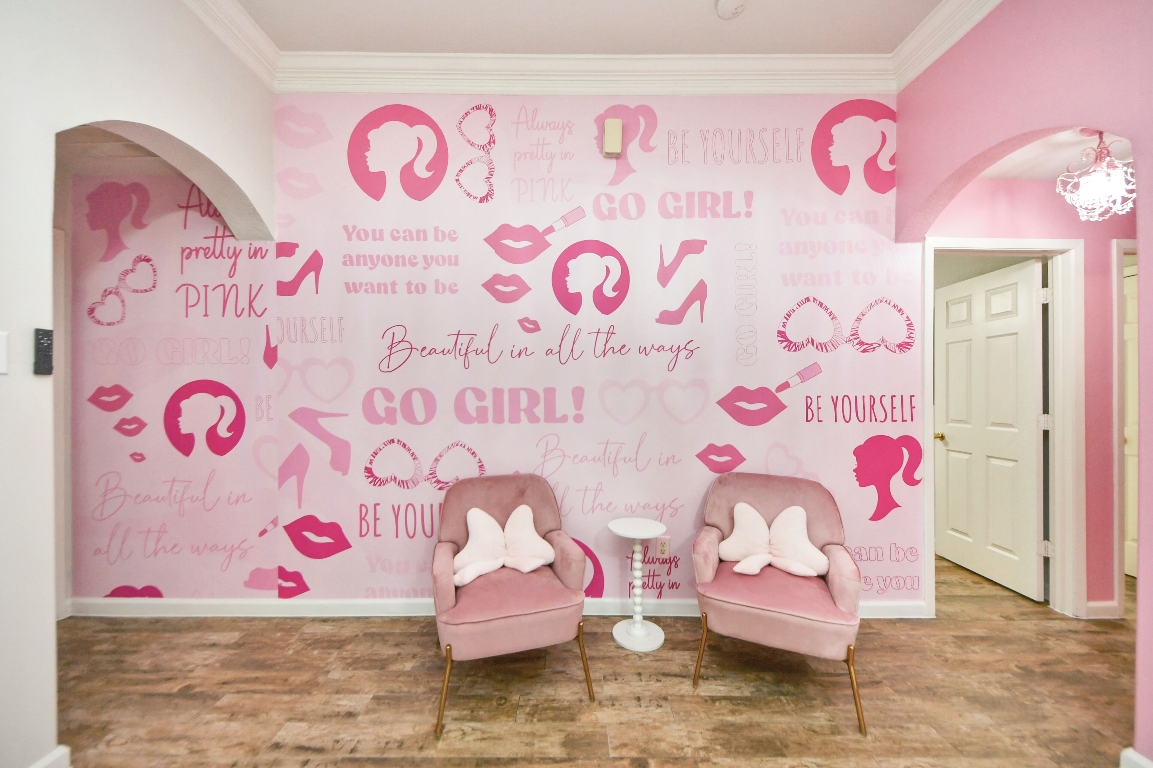 A room with pink walls, two pink armchairs, a small white table, and a door.