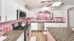 A kitchen with white cabinets, a stainless steel microwave, a gas stove, and a ceiling fan.