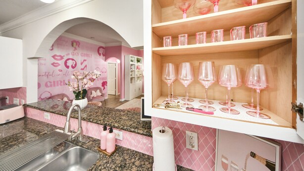 A kitchen with pink accents, a sink, and a wine display with pink glasses.