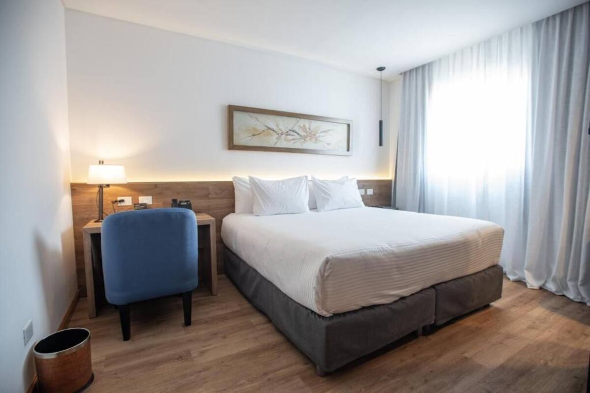 Een hotelkamer met een bed, een bureau, een stoel, een lamp en een schilderij aan de muur.