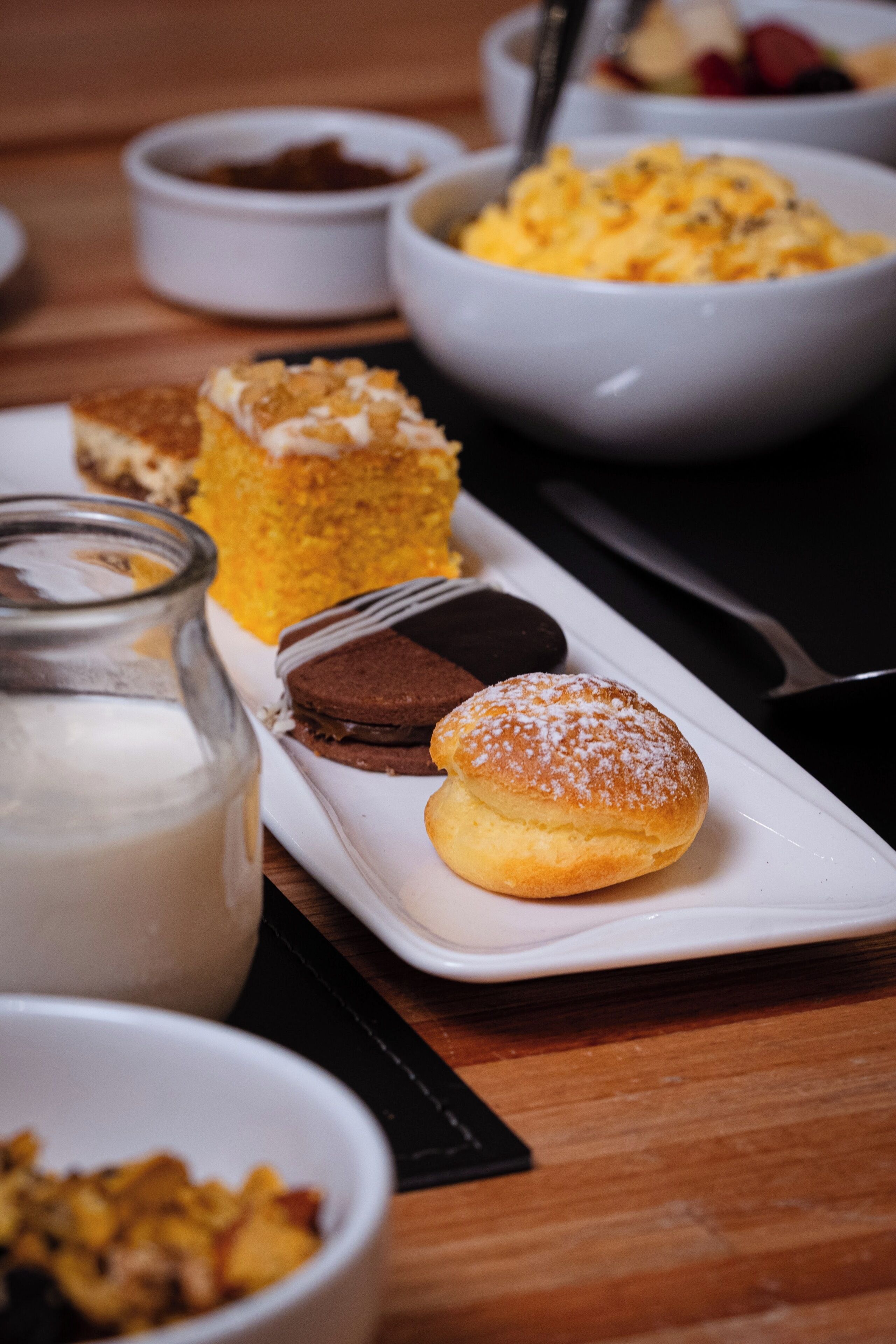 A variety of desserts on a white plate, including a chocolate cake, a yellow dessert, and a powdered bun.