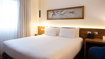 Quarto de hotel com uma cama grande, mesa de cabeceira com telefone e um quadro na parede.