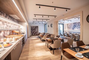 A modern dining area with a buffet on the left, multiple tables and chairs arranged for dining, and a large window providing natural light.